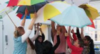 junge Menschen stecken die Köpfe zusammen und heben gemeinsam bunte Regenschirme nach oben, sie sind im Innenraum, Quelle: DTF