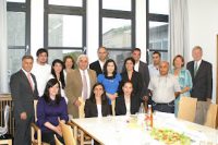 Gruppenbild offiziell angezogener Menschen an einem Tisch vor vier großen Fenstern, Quelle: DTF