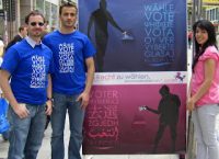 zwei Männer in blauen T-Shirts neben blauem und pinken Wahlposter, links von ihnen ist eine Frau im pinken T-Shirt, Quelle: DTF