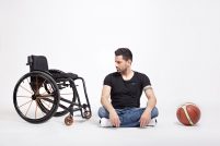 Mann sitzt im Schneidersitz auf dem Boden, rechts ein Rollstuhl, links ein Basketball, Quelle: Angela Wulf, Fotograf/in: Angela Wulf